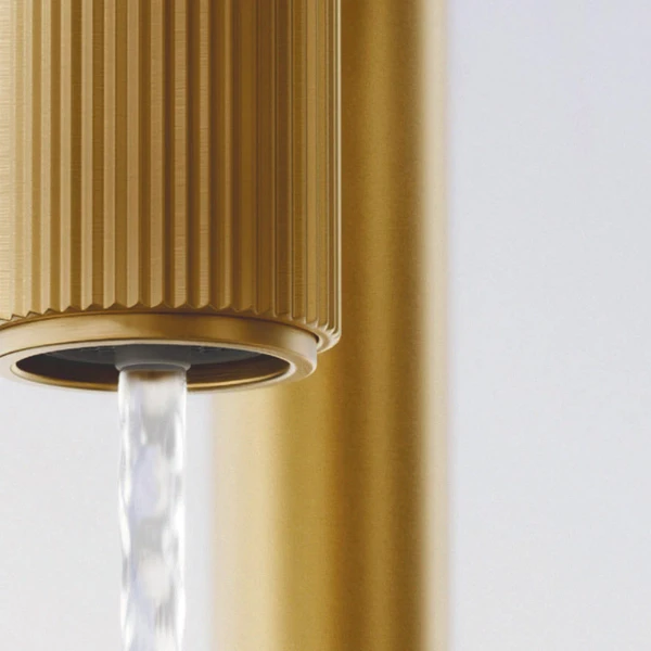 Gold brushed kitchen tap SWITCH with ribbed spout, from which water flows.